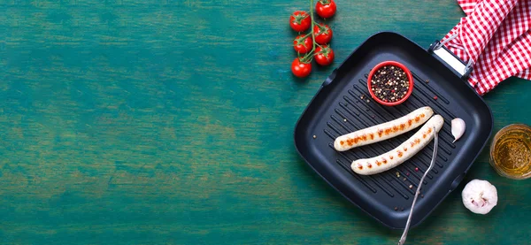 White grilled sausages with black pepper, fresh tomatoes and fresh cold beer in a grill pan on an old vintage green wooden background with free place for text, top view, horizontal