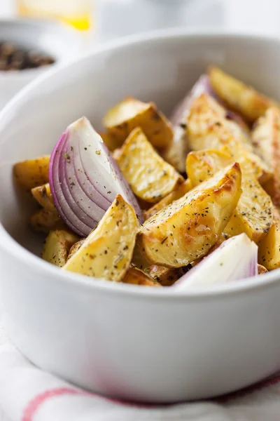 Batata de corte assada no forno com cebola vermelha e ervas italianas, rústica, vintage ou estilo country em uma tigela redonda com guardanapo branco em um velho fundo de madeira vintage, close-up — Fotografia de Stock