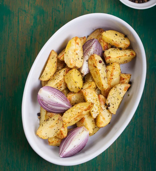 Patata cortada al horno con cebolla roja y hierbas italianas, estilo rústico, vintage o rústico en un tazón redondo sobre un antiguo fondo de madera verde vintage, vista superior, con espacio libre para texto — Foto de Stock