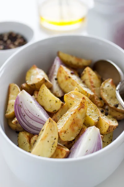 Oven-baked cut potato with red onion and Italian herbs, rustic, vintage or country style in a round bowl with white napkin on an old vintage wooden background, closeup — 图库照片