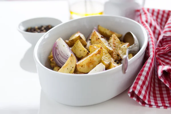 Oven-baked cut potato with red onion and Italian herbs, rustic, vintage or country style in a round bowl with white napkin on an old vintage wooden background, closeup — Φωτογραφία Αρχείου