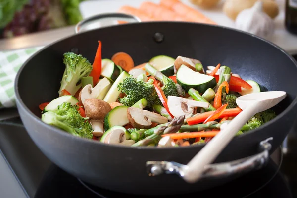 Wok stir fry vegetables with zucchini, spring asparagus, paprika, carrot and broccoli, closeup in a wok pan in a kitchen, selective focus