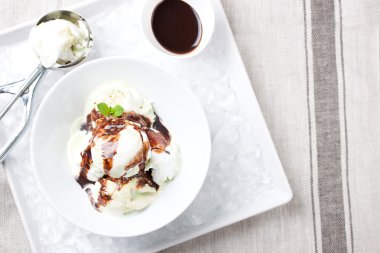 Vanilya ve fıstık lı dondurma çikolata soslu bir kase de buzile bir tabakta