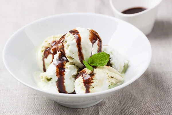 Helado de vainilla y pistacho con salsa de chocolate en un tazón en un plato sobre un textil de lino — Foto de Stock