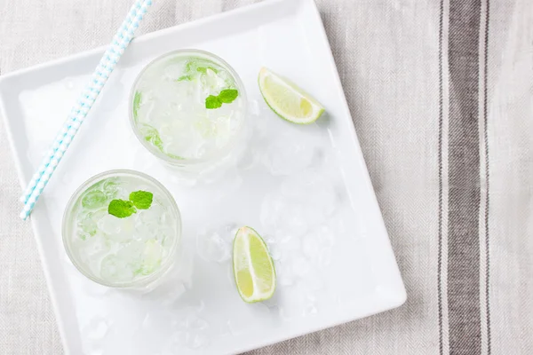 Cocktail di mojito freddo analcolico con lime fresco, menta e ghiaccio tritato su un piatto bianco — Foto Stock
