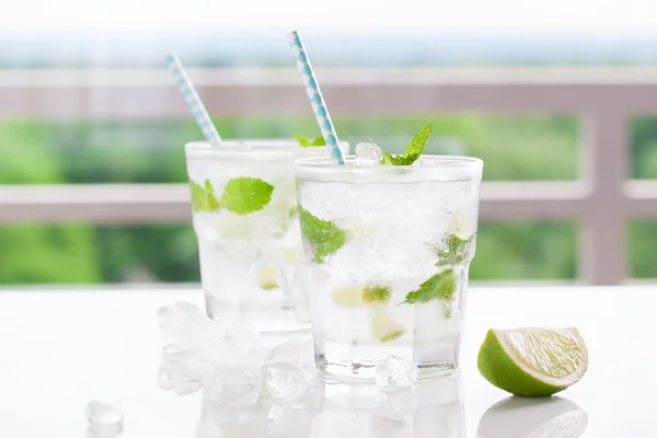 Cóctel de mojito frío sin alcohol con lima fresca, menta y hielo picado sobre una mesa blanca — Foto de Stock