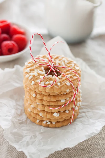 Biscoitos com baixas de açúcar e fita vermelha em uma chapa branca com framboesas em um contexto em um tecido de linho — Fotografia de Stock