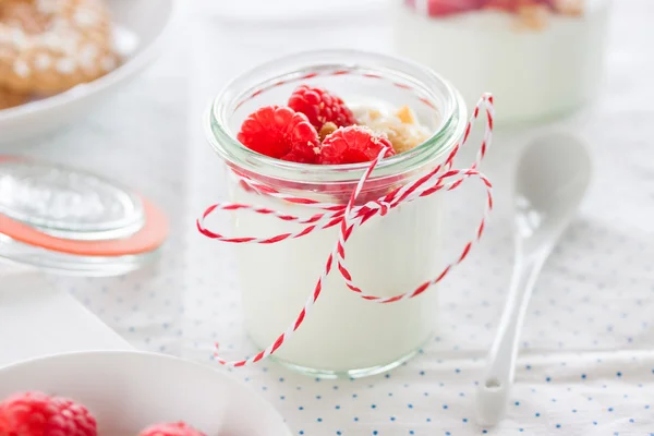Domowy deser jogurtowy z malinami i kruszonym ciasteczkami w małym słoiku na tle kuchni — Zdjęcie stockowe