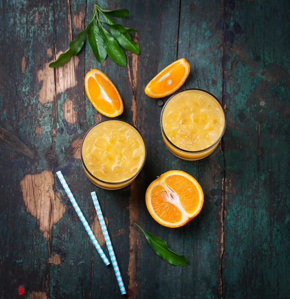 Свежий апельсиновый сок со льдом и свежими апельсинами и голубыми соломинками на старом винтажном экзотическом фоне — стоковое фото