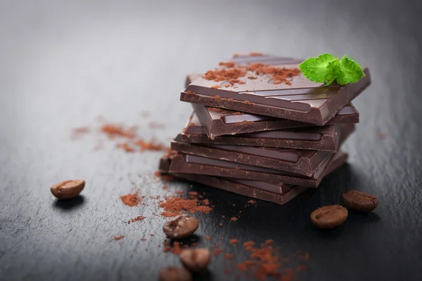 Пачка шоколадных кусочков на темном каменном фоне с какао — стоковое фото