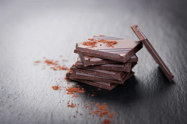 Пачка шоколадных кусочков на темном каменном фоне с какао — стоковое фото