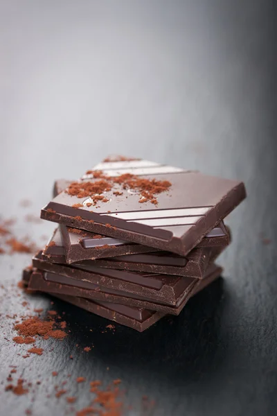 Stapel chocolade stukjes op een donkere stenen achtergrond met cacao — Stockfoto