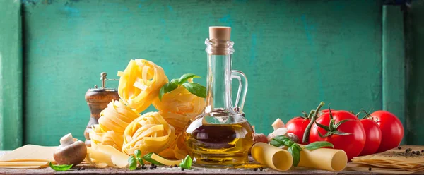 Sfondo alimentare o concetto sano con olio d'oliva, basilico fresco, tagliatelle di pasta, funghi, pomodori e pepe su fondo di legno — Foto Stock