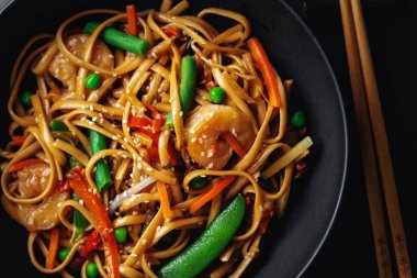 Karides ve sebzeli Asya erişteleri koyu arka planda kasede servis edilir.. 