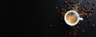 Tasty steaming espresso in cup with coffee beans. View from above. Dark background.  clipart
