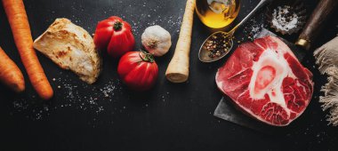 Koyu arka planda kemik ve sebzeli çiğ biftek ve sebze. Üst Manzara. Yemek pişirme konsepti