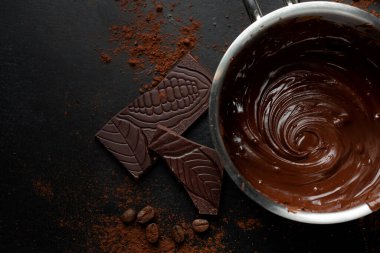 Esmer arka planda çikolata parçaları olan bir tencerede erimiş çikolata. Üst Görünüm. 