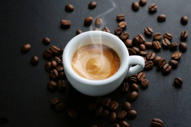 Kahve çekirdekleri ve kaşıkla servis edilen fincanda nefis bir espresso. - Yakın çekim. Koyu arkaplan. 