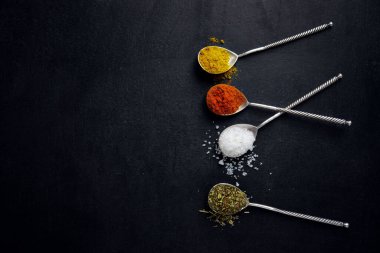 Koyu arka planda kaşıklardaki lezzetli rengarenk baharatlar. Üst Görünüm. 