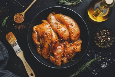Koyu arka planda marine edilmiş çiğ tavuk göğsü ve pişirmeye hazır baharatlar.. 