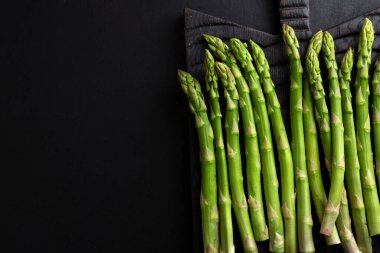 Koyu arkaplanda pişmeye hazır yeşil kuşkonmaz. Yukarıdan görüntüle. 