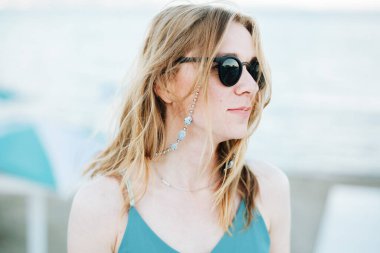 Sahilde arka planda güneş gözlüklü, gülen genç beyaz kadın portresi.. 