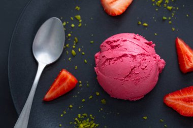 Meyveli çilekli dondurma kepçeleri ve çilek sosu tabakta meyve ve pistacchio ile servis ediliyor. Üst Görünüm. 