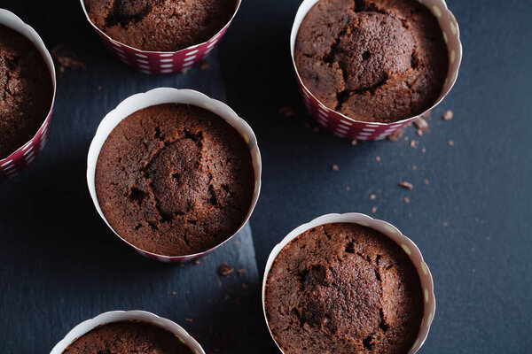 Tasty appetizing chocolate muffins in cups on dark background. 