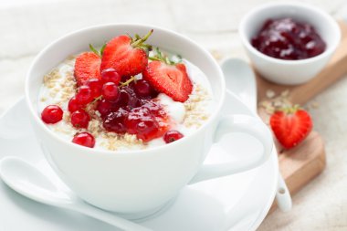 Oatmeal and fruits in white cup with spoon on wooden board for breakfast