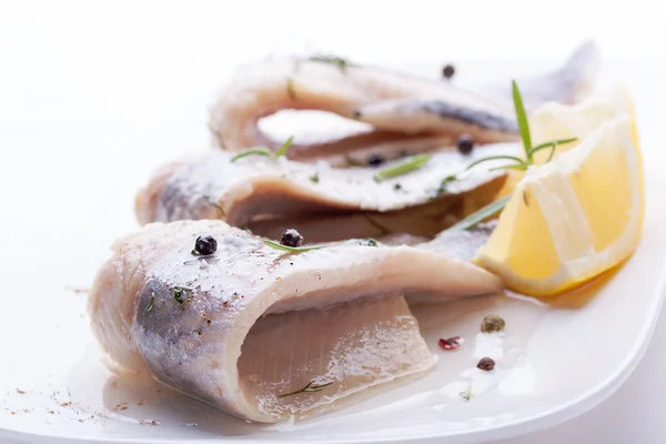 Aringa con sale, pepe, erbe aromatiche e limone su piatto di ceramica bianca su fondo bianco — Foto Stock