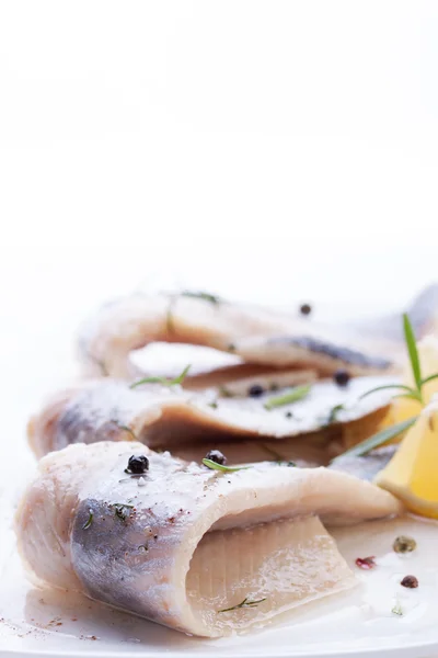 Arenque com sal, pimenta, ervas e limão em placa de cerâmica branca no fundo branco — Fotografia de Stock