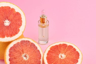 Cam şişedeki narenciye yağı pembe arka planda taze ve sulu greyfurtlar. Spa konsepti.