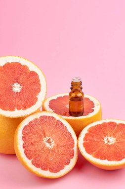 Şişedeki turunçgil yağı ve pembe arka planda taze greyfurt. Güzellik ve sağlık hizmetleri kavramı.