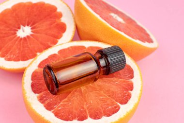 Pembe arka planda greyfurt yarımları üzerinde saf greyfurt yağı bulunan bir şişe. Aromaterapi tedavi kavramı.