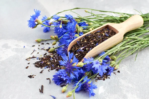 Black tea mix with dried cornflower petals and thyme in wooden scoop, fresh cornflowers bouquet. Herbal tea, healthy lifestyle concept.