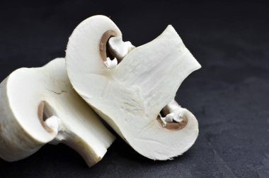 Koyu arka planda taze kesilmiş şampiyon mantarları, pişirmeye hazır. Yakın görünüm.