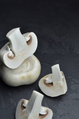 Koyu arkaplanda taze şampiyon mantarları, dilimlenmiş ve bütün, pişirmeye hazır..