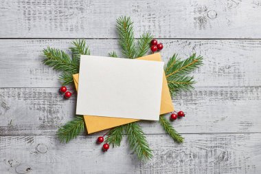 Noel tebrik kartı, köknar ağacı dalları ve ahşap arka planda kırmızı çobanpüsküllü bereler.