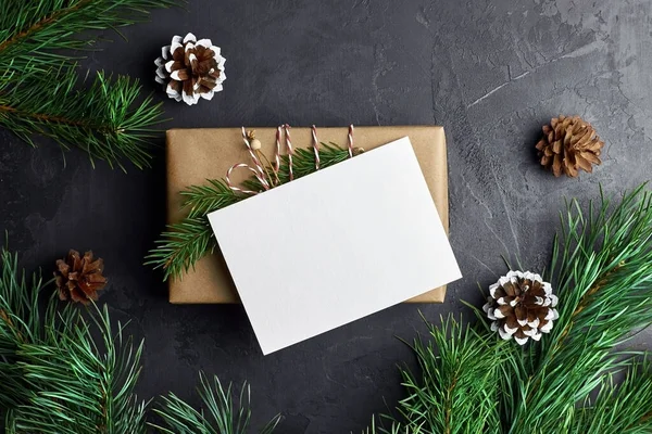 Hediye kutusu ve koyu arkaplanlı kozalaklı çam ağacı dallarıyla Noel kartı maketi. Kış tatilleri kompozisyonu, üst görünüm, düz döşeme, kopyalama alanı.