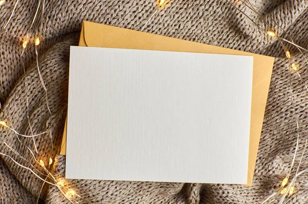 Örgü arka planda çelenk ışıkları olan tebrik kartı modeli. Noel ve Yeni Yıl boş kartı ve içinde kopya alanı olan zarf.