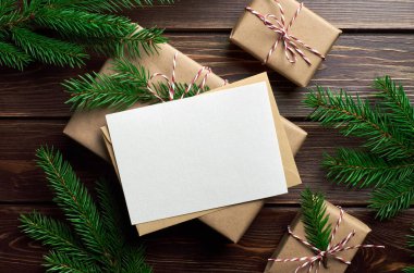 Koyu ahşap arka planda Noel hediyesi kutuları ve köknar ağacı dallarıyla tebrik kartı modeli.