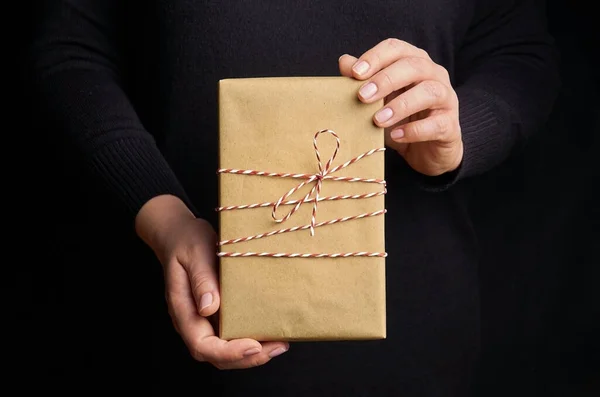 Kobiece Ręce Trzymając Pudełko Świąteczne Zapakowane Papier Rzemieślniczy Czarnym Tle — Zdjęcie stockowe