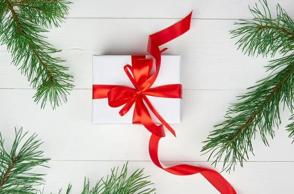 Kerstgeschenkdoos met rood lint en dennenboomtakken op witte houten ondergrond — Stockfoto