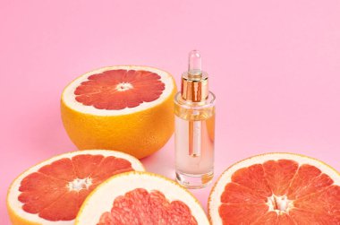 Greyfurt yağı cam şişede greyfurt dilimlerinde pembe arka planda. Aromaterapi kavramı.