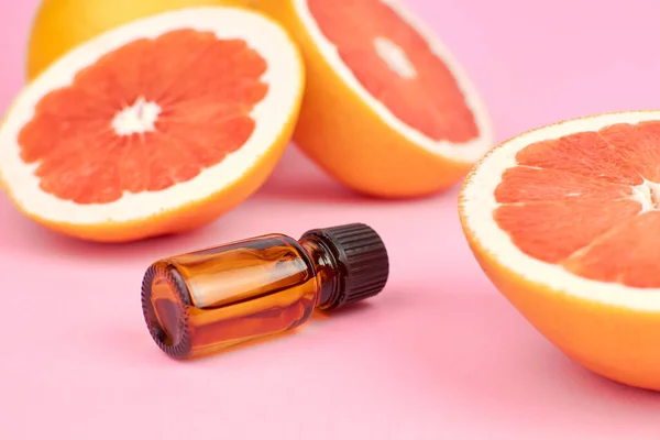 Citrus essential oil in bottle with fresh grapefruit halves on pink background. — Stock Photo, Image
