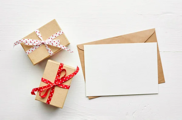 Greeting card mockup and gift boxes with red ribbon on white wooden background, top view, copy space, Valentines day card