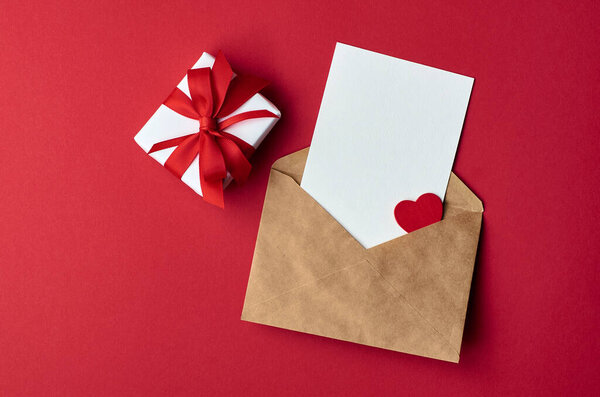 Макет открытки на день Святого Валентина с конвертом и подарочной коробкой с сердцем на фоне красной бумаги