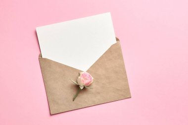 Zarflı ve gül çiçekli tebrik kartı, pembe arkaplanda kopya alanı olan maket.