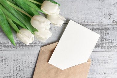 Tahta arka planda lale çiçeği buketi ve zarflı tebrik kartı modeli.