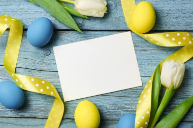 Paskalya bayramı tebrik kartı. Üzerinde lale çiçekleri ve ahşap arka planda renkli yumurtalar var.